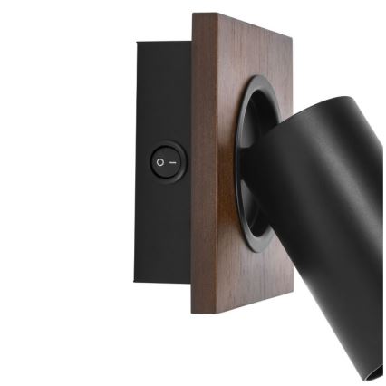 Čierna nástenná lampa s valcovým tienidlom je pripevnená na drevenom štvorcovom podstavci. Lampa má integrovaný vypínač.