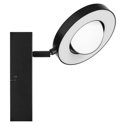 Čierna nástenná lampa s okrúhlou hlavicou svieti. Hlavica je otočná a má biely svetelný kruh. Lampa je pripevnená k stene čiernou montážnou doskou.