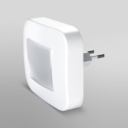 Biela nočná lampa s integrovanou zástrčkou svieti. Je umiestnená na svetlomodrom podklade.