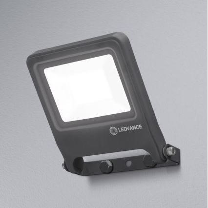 LED reflektor svieti. Je pripevnený na sivú stenu pomocou skrutiek. Na reflektori je logo LEDVANCE.