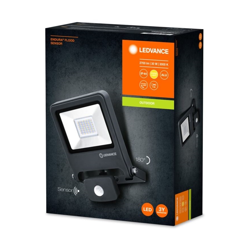 LED reflektor s pohybovým senzorom je pripevnený na stenu. Balenie udáva parametre: 2700 lm, 30 W, 3000 K, IP44, hliníkové puzdro, 180° detekčný uhol, 3-ročná záruka.