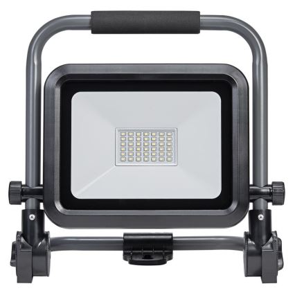 LED pracovné svetlo s rúčkou a nastaviteľným stojanom svieti. Svetlo je umiestnené na čiernom a sivom kovovom ráme.