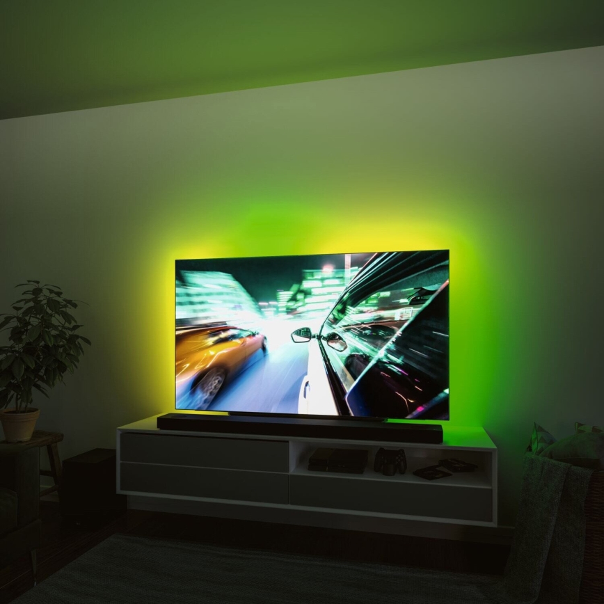 Televízor zobrazuje rýchlu jazdu áut v meste. Je umiestnený na televíznom stolíku v miestnosti so zeleným podsvietením. Na stolíku sú ďalšie elektronické zariadenia.