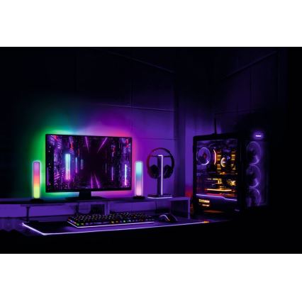 Herný počítač s farebným podsvietením je umiestnený na stole s klávesnicou a myšou. Monitor zobrazuje abstraktnú grafiku. Bočné RGB osvetlenie dopĺňa priestor.