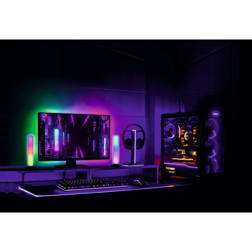 Herný počítač s farebným podsvietením je umiestnený na stole s klávesnicou a myšou. Monitor zobrazuje abstraktnú grafiku. Bočné RGB osvetlenie dopĺňa priestor.