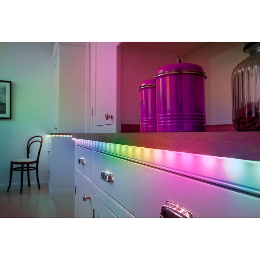 LED pásik svieti farebne pozdĺž kuchynskej linky. Na linke stoja dve fialové dózy. V pozadí je vidieť stoličku a časť kuchyne.