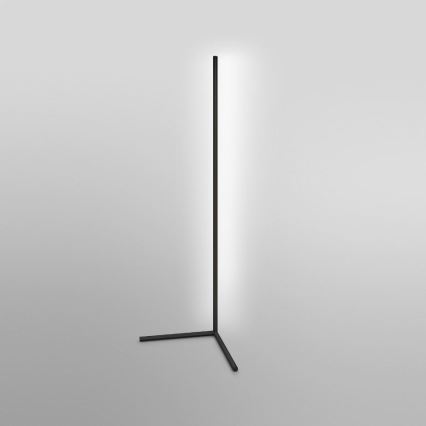 Stojaca lampa svieti. Má vysoký čierny stĺpik a trojnohý podstavec. Nachádza sa na svetlej podlahe.