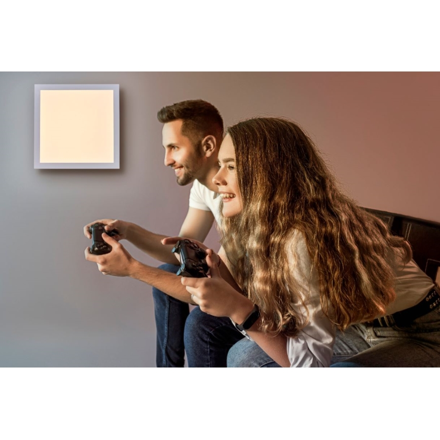 Pár hrá hru na hernom ovládači, sedí na posteli v miestnosti so štvorcovou nástennou lampou.