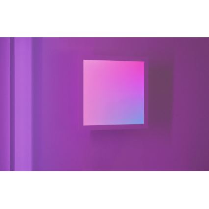 Svetelný panel s prechodom farieb od ružovej po modrú je umiestnený na fialovej stene. Panel je obdĺžnikového tvaru a je vsadený do svetlejšej rámu. Stena je osvetlená tlmeným svetlom.