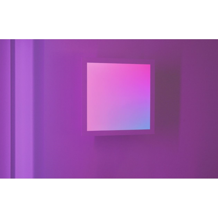 Svetelný panel s prechodom farieb od ružovej po modrú je umiestnený na fialovej stene. Panel je obdĺžnikového tvaru a je vsadený do svetlejšej rámu. Stena je osvetlená tlmeným svetlom.