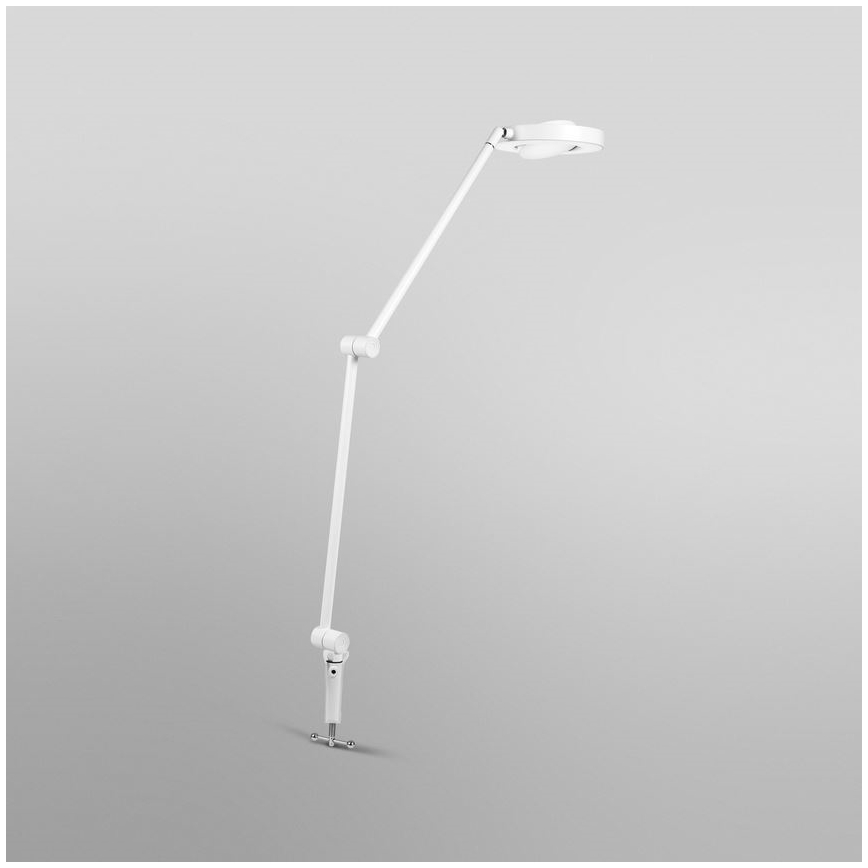 Biela stolová lampa s okrúhlou hlavou sa nachádza na svetlosivom pozadí. Lampa je na kĺbovej nohe, ktorá umožňuje nastavenie výšky a smeru svetla.