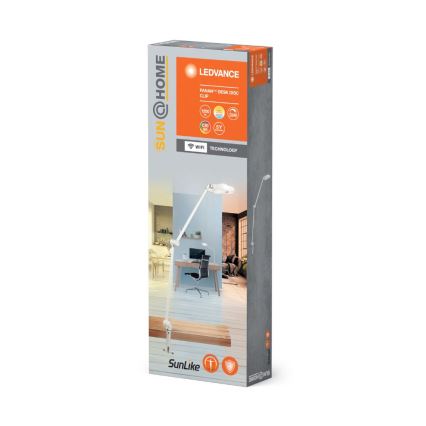 Balenie stolovej LED lampy s nastaviteľným ramenom na upevnenie na stôl alebo stenu. Lampa je zobrazená v interiéri pri pracovnom stole. Na obale je uvedené: LEDVANCE, PANAM™ DESK DISC CLIP, 1000 lm, DIM, CRI 90, 5Y, WiFi TECHNOLOGY.