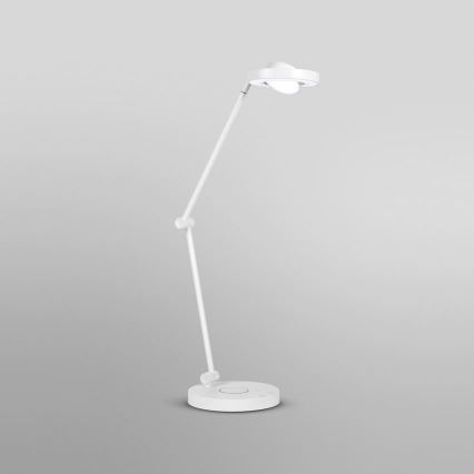 Biela stolová lampa s nastaviteľným ramenom svieti. Nachádza sa na svetlošedom pozadí.