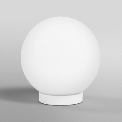 Biela guľová lampa stojí na malej bielej podstavci. Lampa je umiestnená na svetlosivom pozadí.
