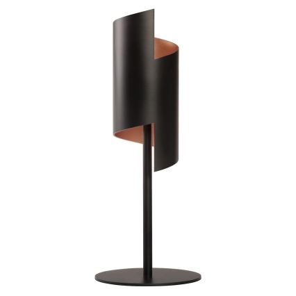 Stolová lampa s čiernym valcovým tienidlom, čiastočne obtočeným medeným pásikom, stojí na tenkej čiernej kovovej nohe s kruhovou základňou.