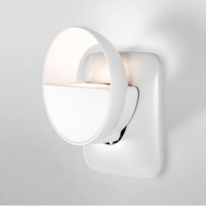 Biela nočná lampa v tvare polkruhu svieti. Zariadenie je zapojené do bielej elektrickej zásuvky na stene.