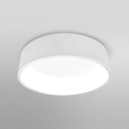 Biela stropná lampa svieti na sivom strope. Lampa má valcový tvar s vnútorným kruhovým difúzorom.