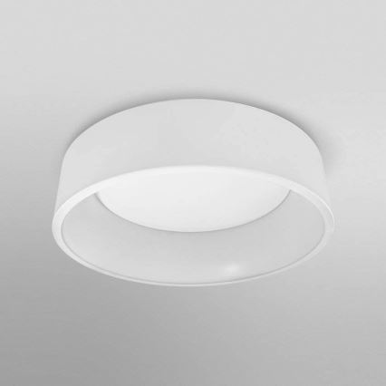 Biela kruhová stropná lampa je pripevnená k stropu. Svietidlo je zapustené do stropu a má vnútorný okrúhly difúzor. Lampa je osvetlená.