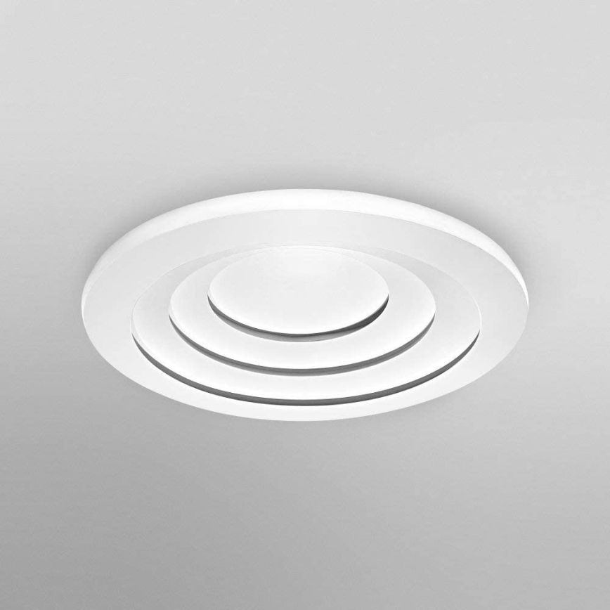 Biely kruhový ventilačný otvor s koncentrickými kruhmi je namontovaný na svetlom strope.