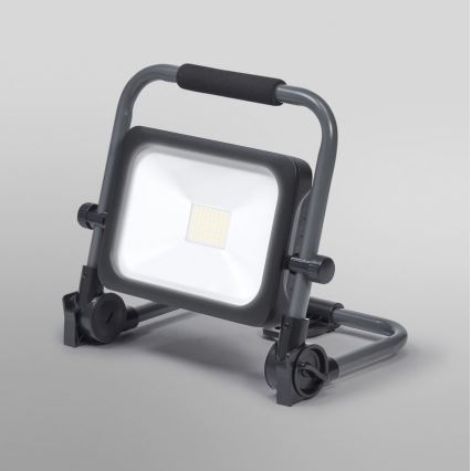 Prenositelná LED pracovná lampa svieti na sivom podklade. Lampa je umiestnená na sklopnom stojane s kolieskami a rukoväťou.