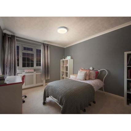 Svietidlo svieti v detskej izbe. Izba obsahuje posteľ s šedou prikrývkou, písací stôl a knihovňu. Steny sú tmavosivé.