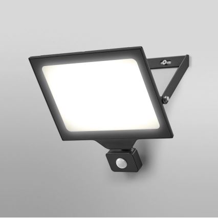 Čierna nástenná LED lampa s pohybovým senzorom svieti. Je pripevnená na svetlej stene. Lampa má obdĺžnikový tvar s jasným bielym svetlom.