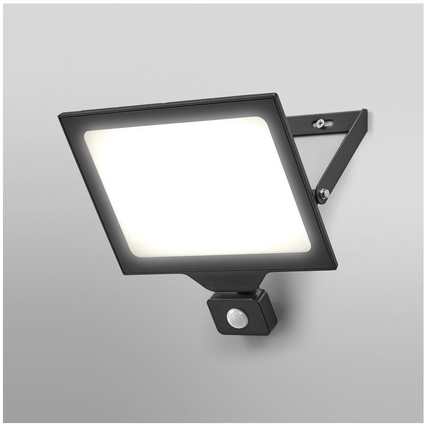 Čierna nástenná LED lampa s pohybovým senzorom svieti. Je pripevnená na svetlej stene. Lampa má obdĺžnikový tvar s jasným bielym svetlom.