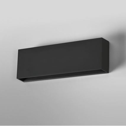 Dlhá obdĺžniková čierna nástenná lampa je pripevnená k stene. Svietidlo je umiestnené horizontálne. Jednoduchý dizajn s úzkym otvorom na spodnej strane.