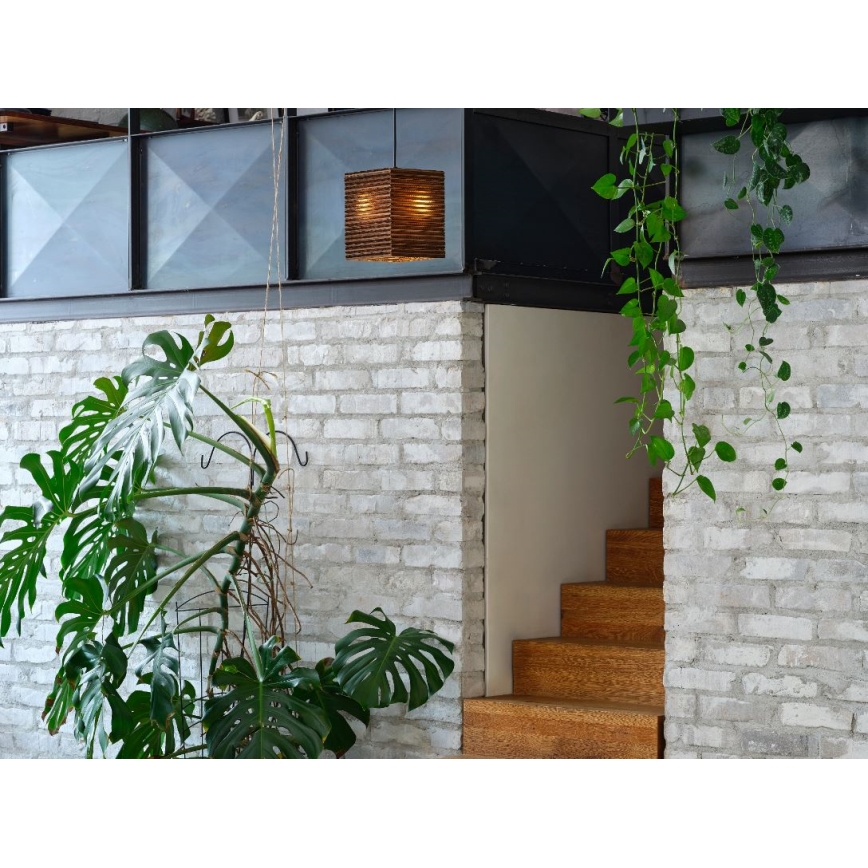 Drevená lampa visí v interiéri. Vedľa nej sa nachádza schodisko z dreva a stena z bielych tehál. Popri stene rastú zelené rastliny.
