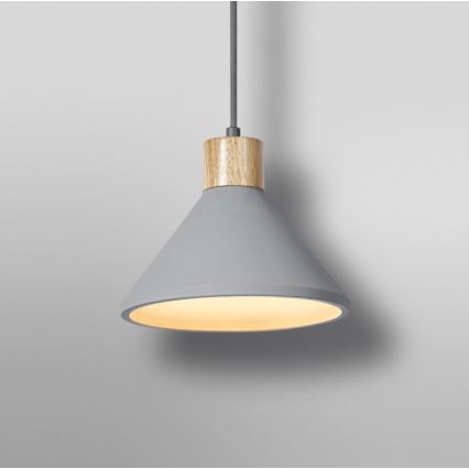 Šedá visutá lampa s dreveným detailom na vrchu svieti na svetlom sivom pozadí. Lampa má kužeľovitý tvar a vnútro je osvetlené teplým svetlom.