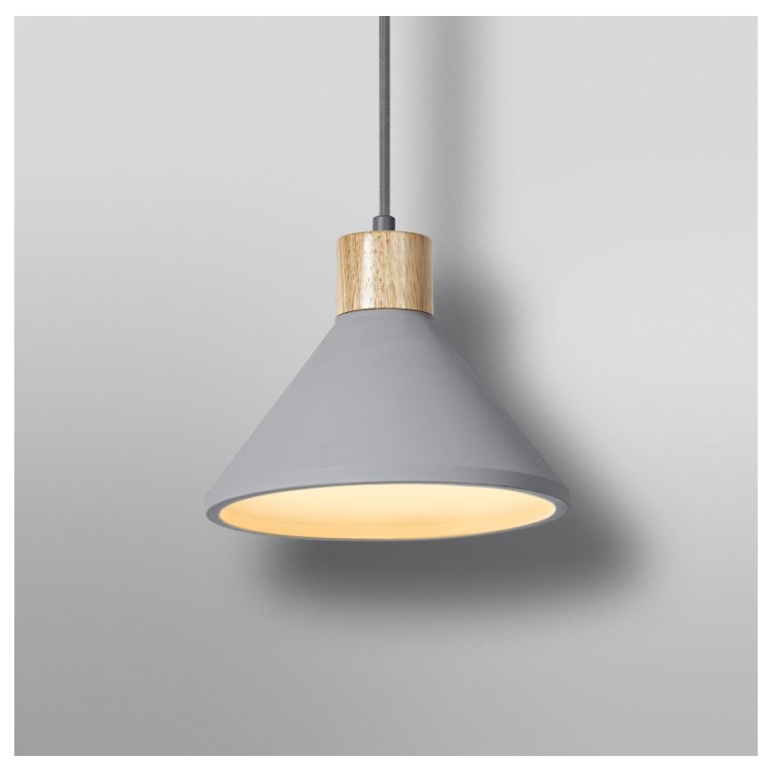 Šedá visutá lampa s dreveným detailom na vrchu svieti na svetlom sivom pozadí. Lampa má kužeľovitý tvar a vnútro je osvetlené teplým svetlom.