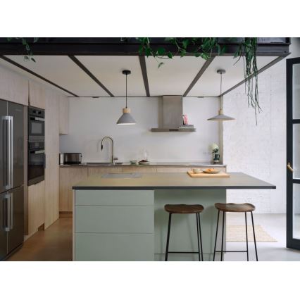 Dve šedé závesné lampy s drevenými detailmi svietia nad kuchynským ostrovčekom s dvoma stoličkami. Ostrovček má svetlosivú pracovnú dosku a svetlozelené skrinky. Kuchyňa je v modernom štýle s drevenými prvkami.