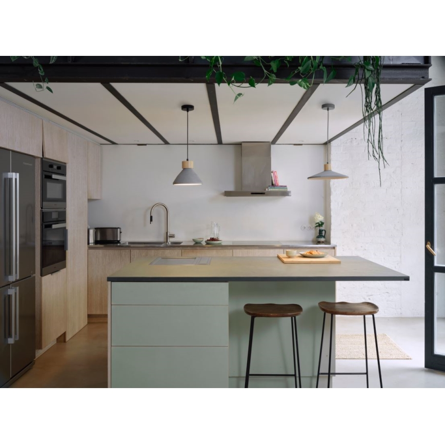 Dve šedé závesné lampy s drevenými detailmi svietia nad kuchynským ostrovčekom s dvoma stoličkami. Ostrovček má svetlosivú pracovnú dosku a svetlozelené skrinky. Kuchyňa je v modernom štýle s drevenými prvkami.