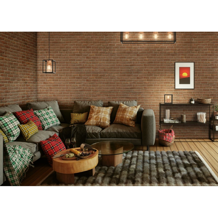 Rohová sedačka s mnohými vankúšmi v kockovanom vzore stojí v miestnosti s tehlovou stenou. Na nízkom drevenom stolíku pred sedačkou sú poháre a ovocie. Na podlahe leží kožušinový koberec. Miestnosť je doplnená nástennou lampou, stropným svietidlom a úzkou poličkou s dekoráciami.