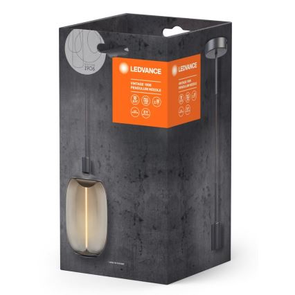 Závesné svietidlo LEDVANCE Vintage 1906 Pendulum Needle je zobrazené v balení. Svietidlo visí na čiernom kábli, má sklenený tienidlo s teplým svetlom. Balenie je tmavosivé s oranžovým popisom.