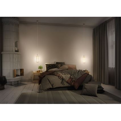 Dve zavesené lampy svietia v spálni. Posteľ je prezlečená, pri posteli je nočný stolík. V pozadí je kachľová pec.