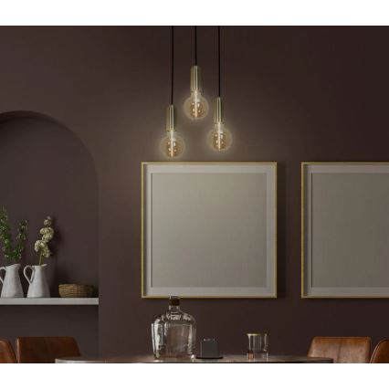 Trojramenné závesné svietidlo s guľovitými tienidlami svieti v tmavej miestnosti. Svietidlo je umiestnené nad stolom s dekoráciami. V pozadí sú obrazy v zlatých rámoch.