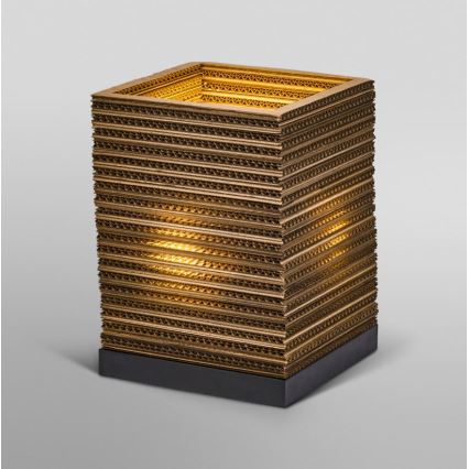 Stolová lampa z prekladaných vrstiev kartónu svieti. Lampa má štvorcový tvar a stojí na tmavej podstavci. Svetlo presvitá cez vrstvy.