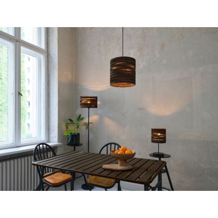 Svietidlá z kartónu svietia v jedálni. Závesné svietidlo je umiestnené nad stolom, stojacia lampa a stolová lampa sú vedľa stola. V pozadí je okno a betónová stena.