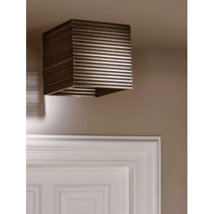 Kubická lampa visí zo stropu. Je vyrobená z vodorovne vrstveného materiálu, ktorý pripomína kartón. Nachádza sa v miestnosti so svetlohnedou stenou a bielymi dverami s výraznými lištami.