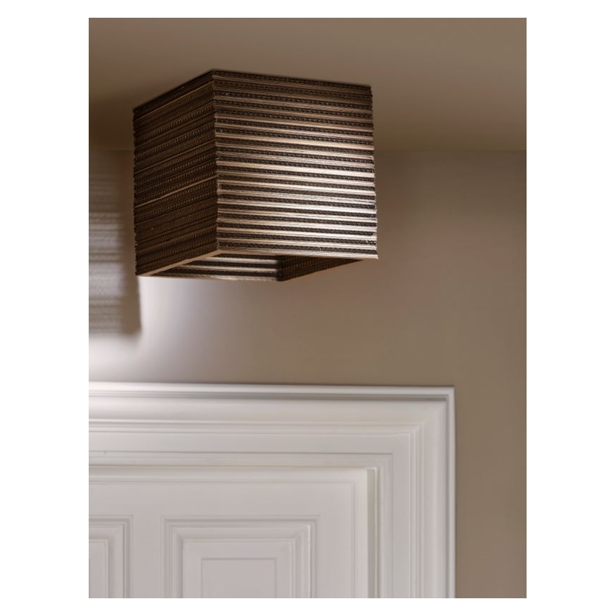 Kubická lampa visí zo stropu. Je vyrobená z vodorovne vrstveného materiálu, ktorý pripomína kartón. Nachádza sa v miestnosti so svetlohnedou stenou a bielymi dverami s výraznými lištami.