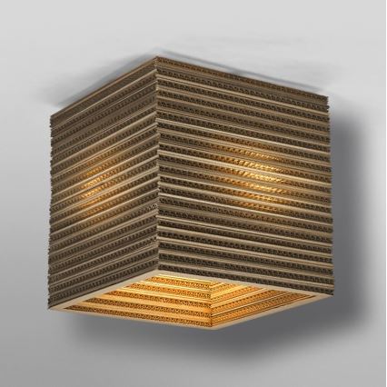 Kubická lampa z vlnitej lepenky svieti. Svetlo presvitá cez vrstvy kartónu. Lampa je pripevnená k stropu.