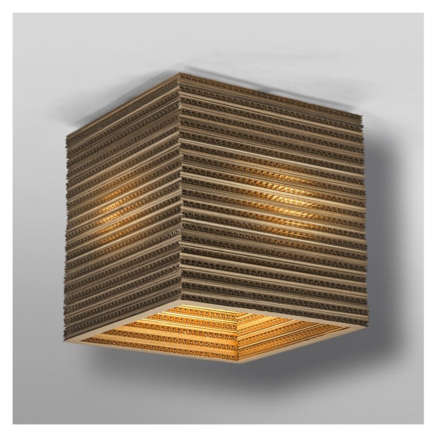Kubická lampa z vlnitej lepenky svieti. Svetlo presvitá cez vrstvy kartónu. Lampa je pripevnená k stropu.