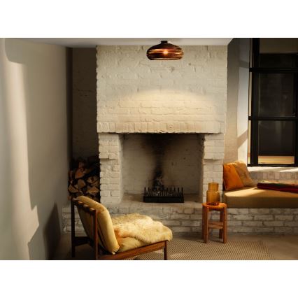 Svietidlo svieti v miestnosti s krbom a sedacím nábytkom. Drevená stolička s kožou je umiestnená pred krbom z bielych tehál. V miestnosti je tiež sedacia lavica a nízky stolík.