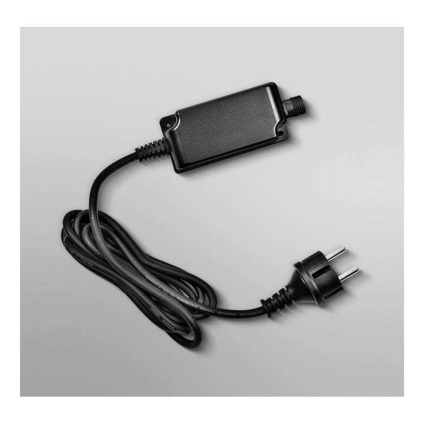 Čierna sieťová zástrčka s káblom je pripojená k malému, obdĺžnikovému, čiernemu adaptéru. Adaptér má výstupný konektor. Leží na svetlošedom podklade.