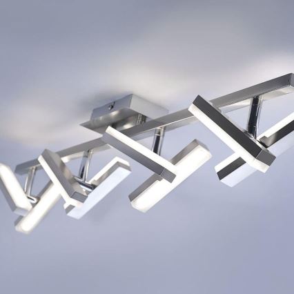 Stropné svietidlo s viacerými ramenami v tvare písmena V s integrovanými LED diódami je pripevnené k stropu. Ramenné sú kovové a striebornej farby. Svietidlo je súčasťou stropnej inštalácie.