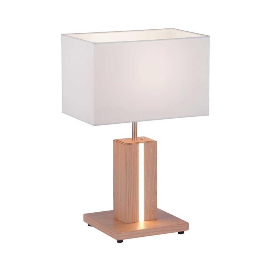 Stolová lampa s bielym textilným tienidlom stojí na drevenom podstavci. Svetlo svieti cez vertikálnu štrbinu v dreve. Lampa je na štvorcovej drevenej základni.