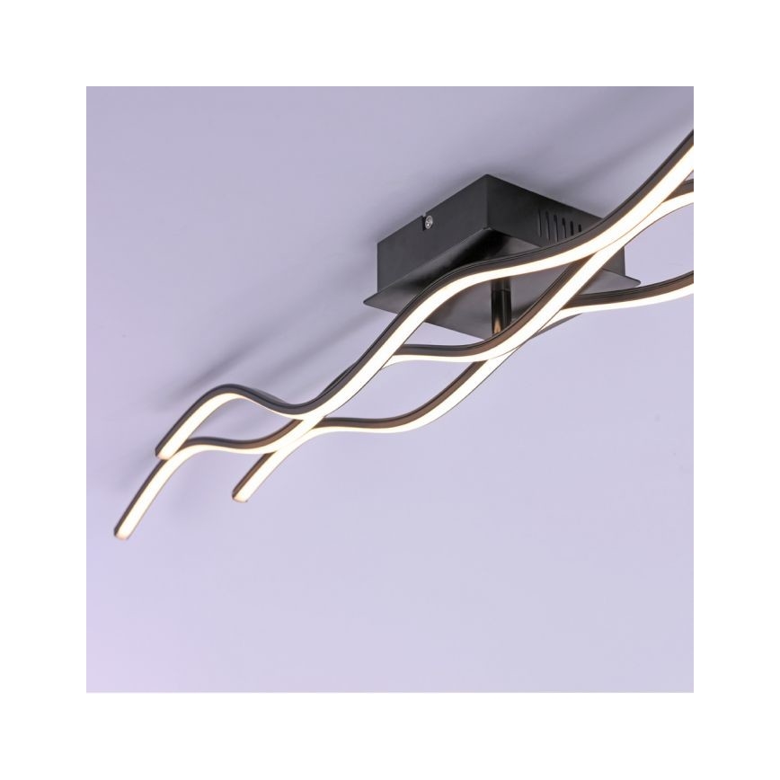 Svietidlo s dvoma vlnovitými LED pásikmi je pripevnené k štvorcovému čiernemu stropnému držiaku. Pásik vyžaruje teplé svetlo. Svetlo je inštalované na strope.