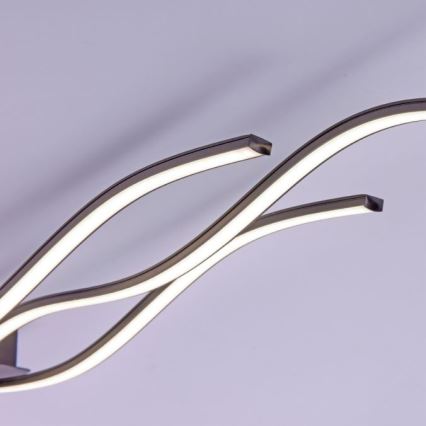 Dve krivolaké LED svietidlá v tvare písmena S svietia proti svetlému pozadiu. Svietidlá sú kovové, tmavosivej farby.