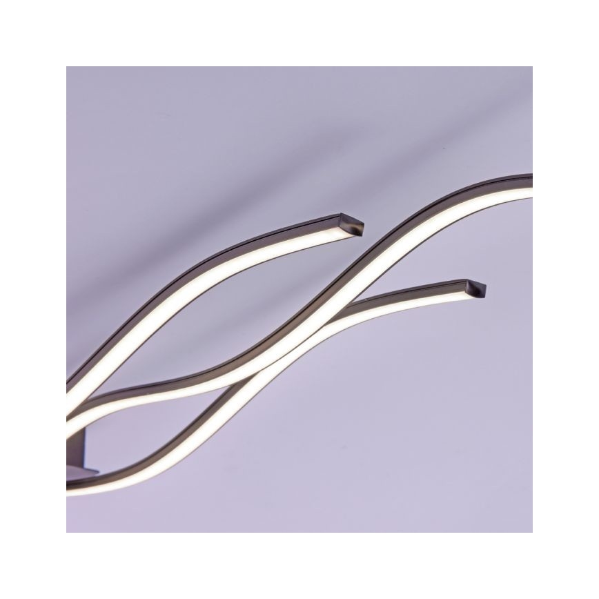 Dve krivolaké LED svietidlá v tvare písmena S svietia proti svetlému pozadiu. Svietidlá sú kovové, tmavosivej farby.